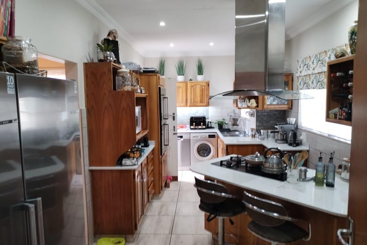 A functional kitchen featuring wooden cabinetry, a central island with a built-in gas hob, stainless steel extractor fan, and tiled flooring.