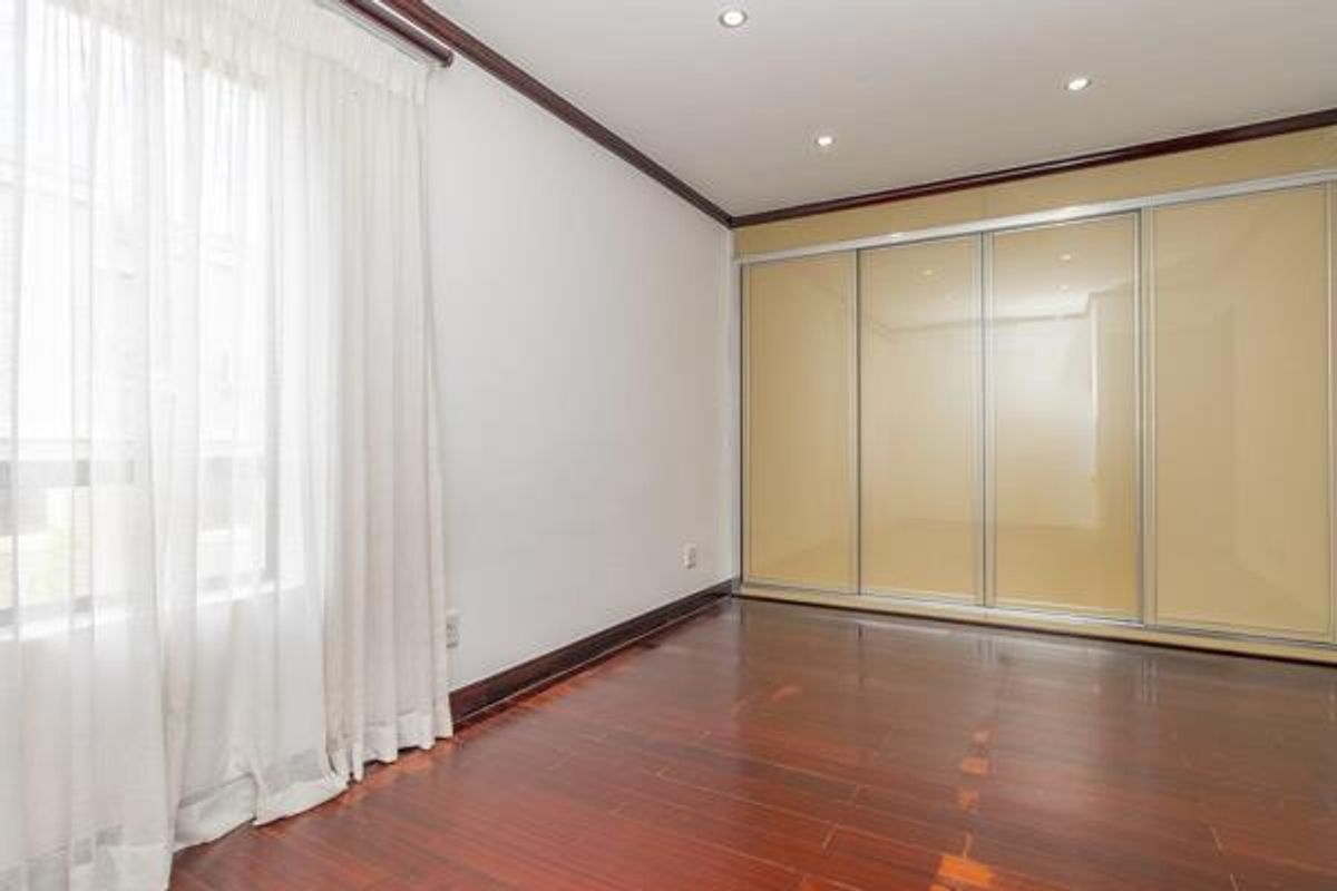 A bright bedroom featuring polished timber flooring, recessed downlighting, and large built-in sliding door wardrobes.