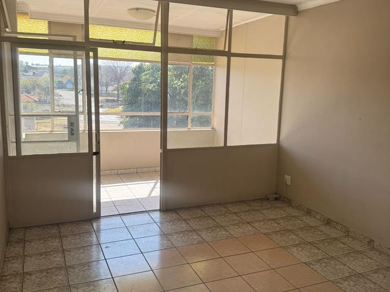 An empty living area featuring tiled flooring and a large glass partition wall leading to an attached balcony space.