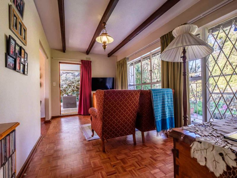 A cozy living room featuring classic parquet flooring, exposed timber ceiling beams, and direct access to an outdoor patio area through sliding glass doors.