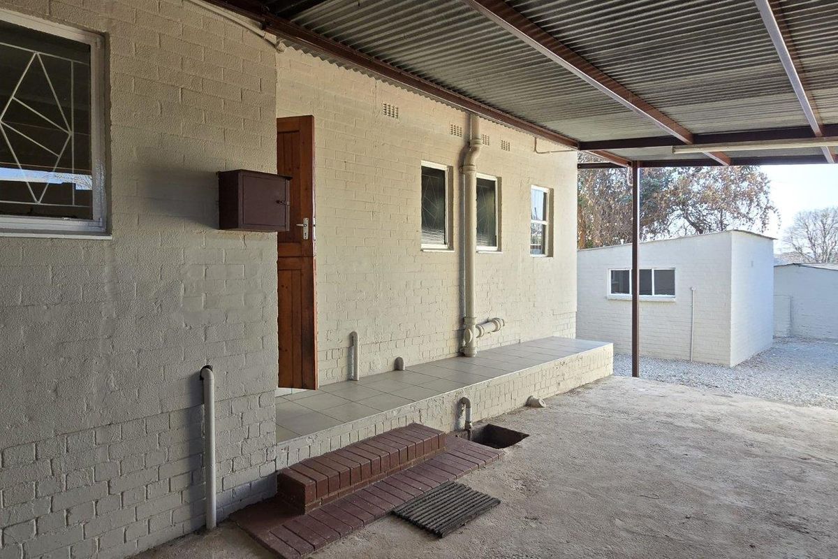 Rear exterior view showing a covered patio area with brick facade, tiled flooring, and corrugated metal roofing.