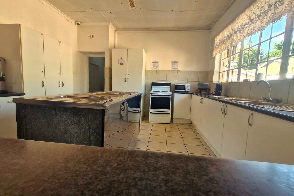A dated kitchen featuring white cabinetry, tiled splashbacks, a central island, and a freestanding stove, offering a functional layout in need of modernization.