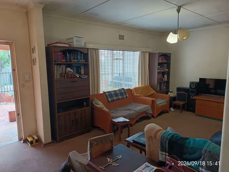 A living room featuring a large window, coving, and carpet flooring, offering a functional space with potential for modernization.