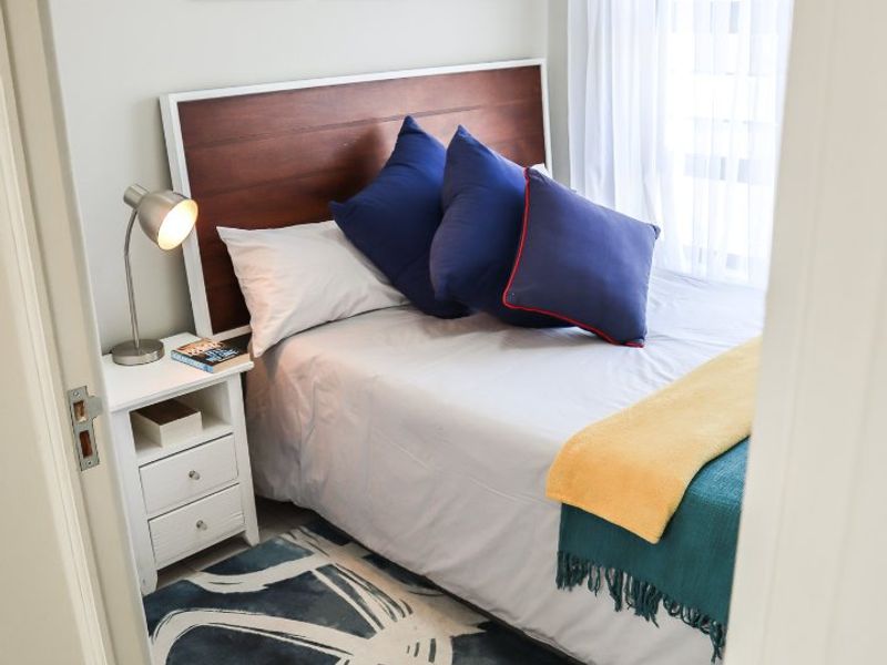 A compact, well-lit bedroom featuring neutral wall tones and a window with sheer curtains, providing a comfortable and functional sleeping space.