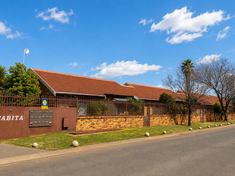 Street view of the Tabita townhouse complex, featuring a brick boundary wall, security fencing, and tiled roof architecture.