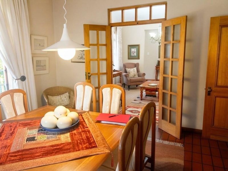 A dining room featuring terracotta floor tiles and classic wooden french doors leading into an adjacent living space.