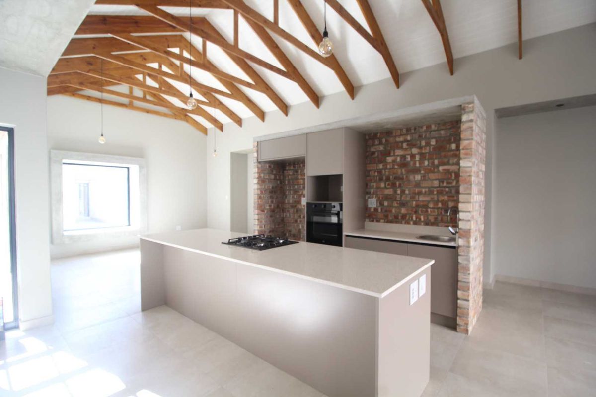 Modern open-plan kitchen featuring a central island with a built-in gas hob, exposed brick accents, and high vaulted timber-trussed ceilings.