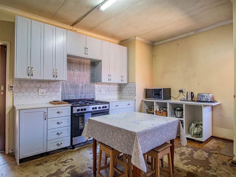 A functional kitchen featuring light-colored cabinetry, a gas stove, and a tiled backsplash, currently requiring updates to the flooring and wall finishes.