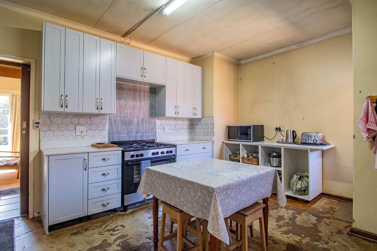 A functional kitchen featuring light-colored cabinetry, a gas stove, and a tiled backsplash, currently requiring updates to the flooring and wall finishes.