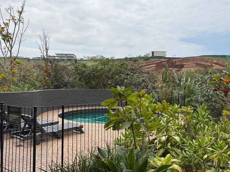 A private swimming pool area featuring a paved deck, secure metal fencing, and a retaining wall, set against a natural landscape backdrop.