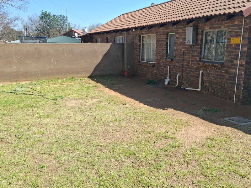 A rear exterior view of a face brick house featuring a tiled roof, boundary wall, and a small garden area.