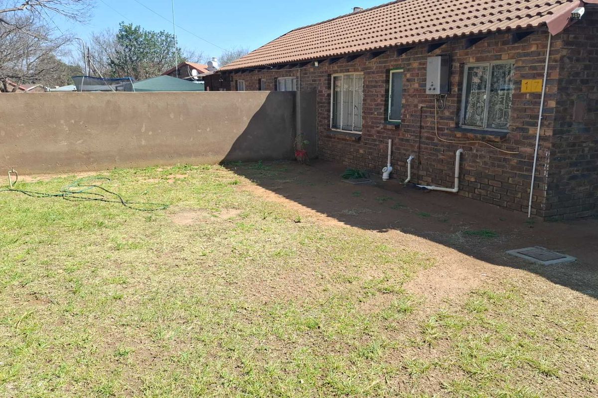 A rear exterior view of a face brick house featuring a tiled roof, boundary wall, and a small garden area.