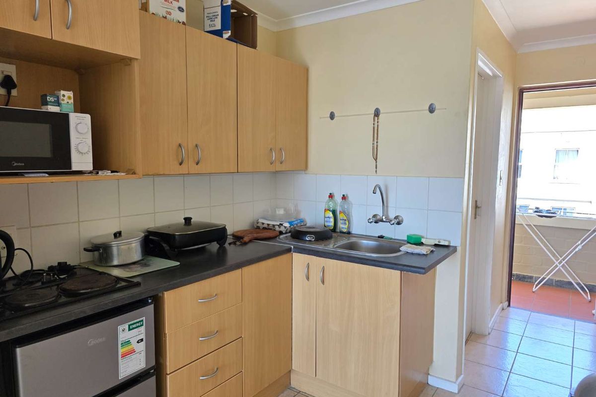 Compact kitchen featuring light wood-look cabinetry, laminate countertops, a stainless steel sink, and a built-in stove, with direct access to an outdoor balcony area.