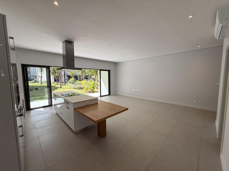 Spacious open-plan living and kitchen area featuring a modern island with integrated hob, recessed lighting, and large sliding doors opening to the garden.