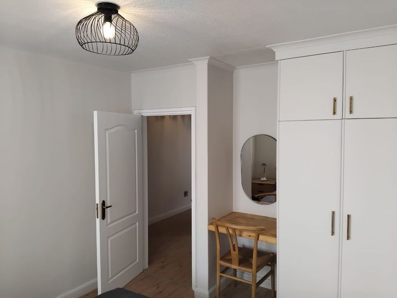 A well-maintained bedroom featuring built-in cupboards, modern laminate flooring, and a stylish pendant light fixture, offering a clean and functional living space.