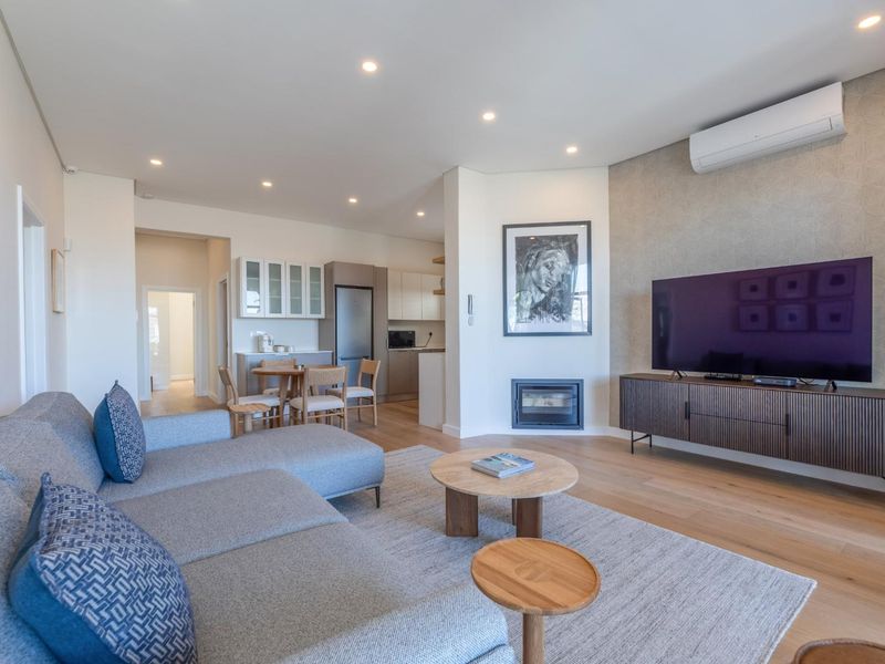 Modern open-plan living area featuring hardwood floors, a built-in fireplace, split-system air conditioning, and a seamless transition to a contemporary kitchen space.