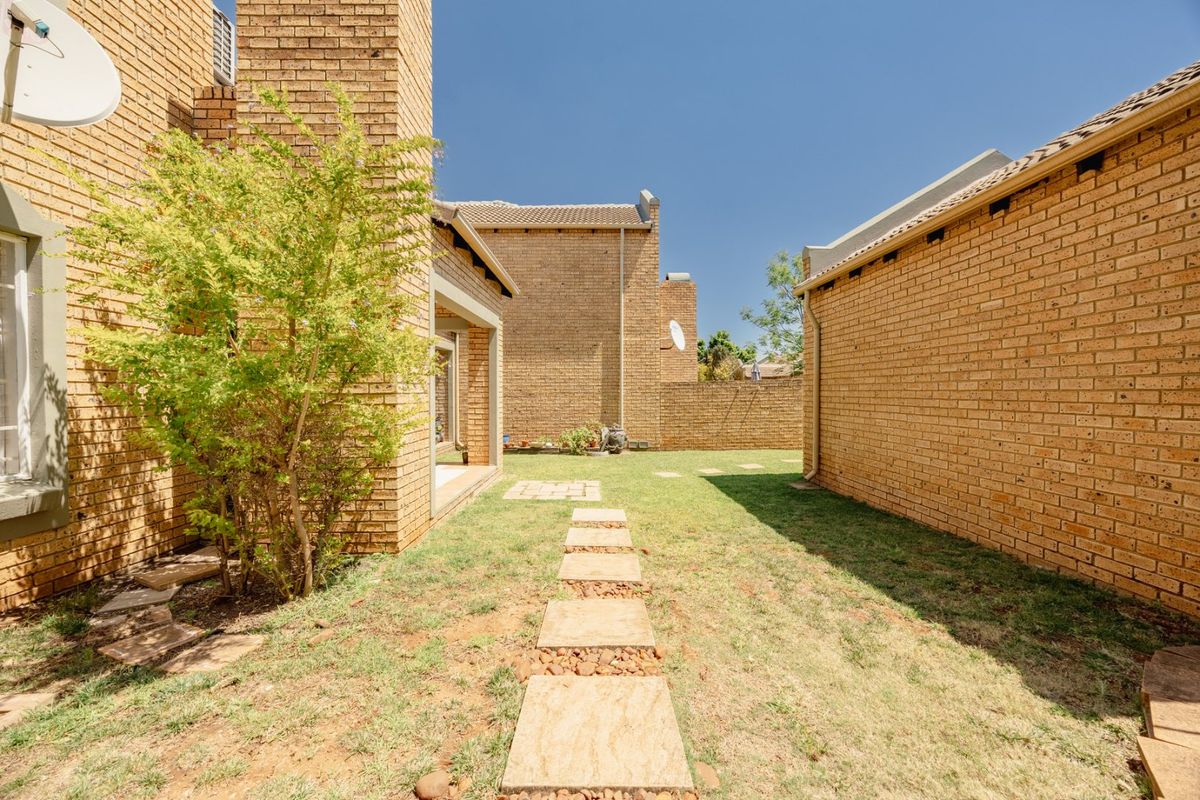 A rear exterior view of the townhouse featuring face brick construction, a stone pathway, and a private garden area.