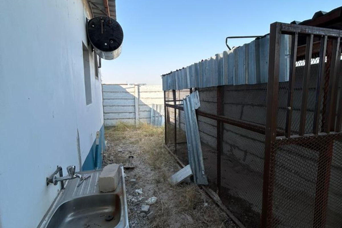 Rear exterior area featuring an external sink, wall-mounted electric geyser, and metal enclosure structure with precast concrete boundary walling.