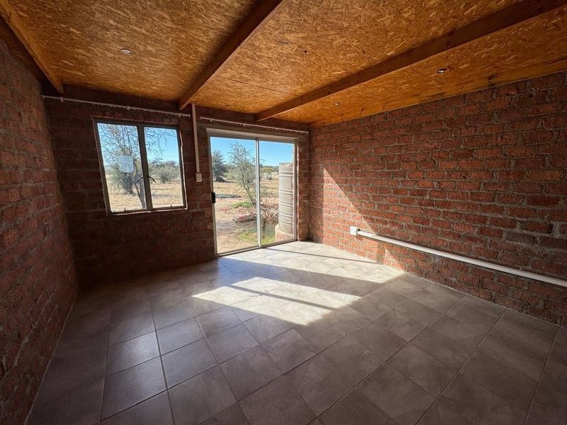 An empty living area featuring exposed brick walls, a timber-look ceiling, tiled floors, and a sliding glass door leading to the exterior.