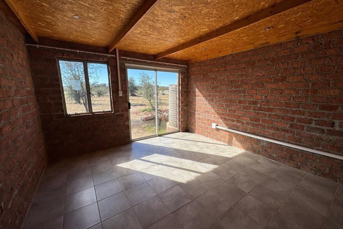 An empty living area featuring exposed brick walls, a timber-look ceiling, tiled floors, and a sliding glass door leading to the exterior.