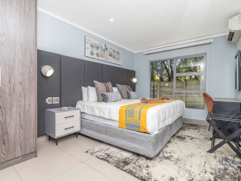 A well-maintained bedroom featuring a built-in wardrobe, upholstered headboard with integrated lighting, tiled floors, and a split-system air conditioning unit.