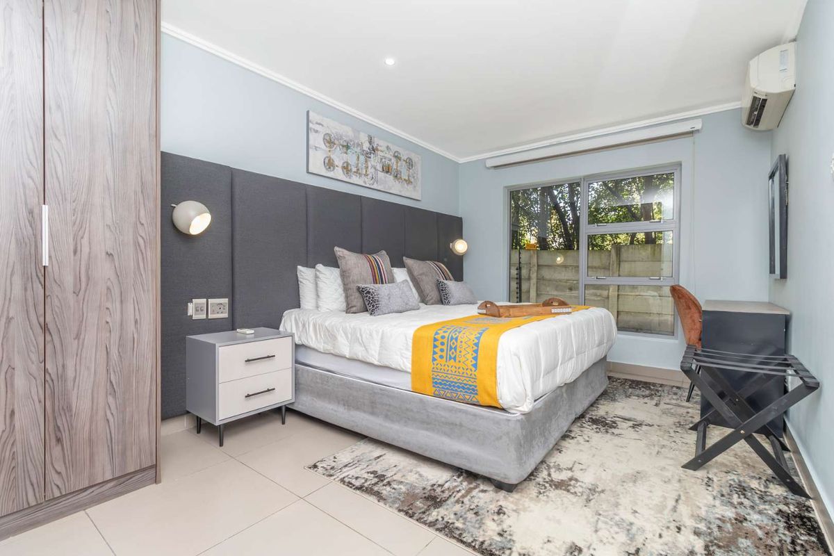 A well-maintained bedroom featuring a built-in wardrobe, upholstered headboard with integrated lighting, tiled floors, and a split-system air conditioning unit.