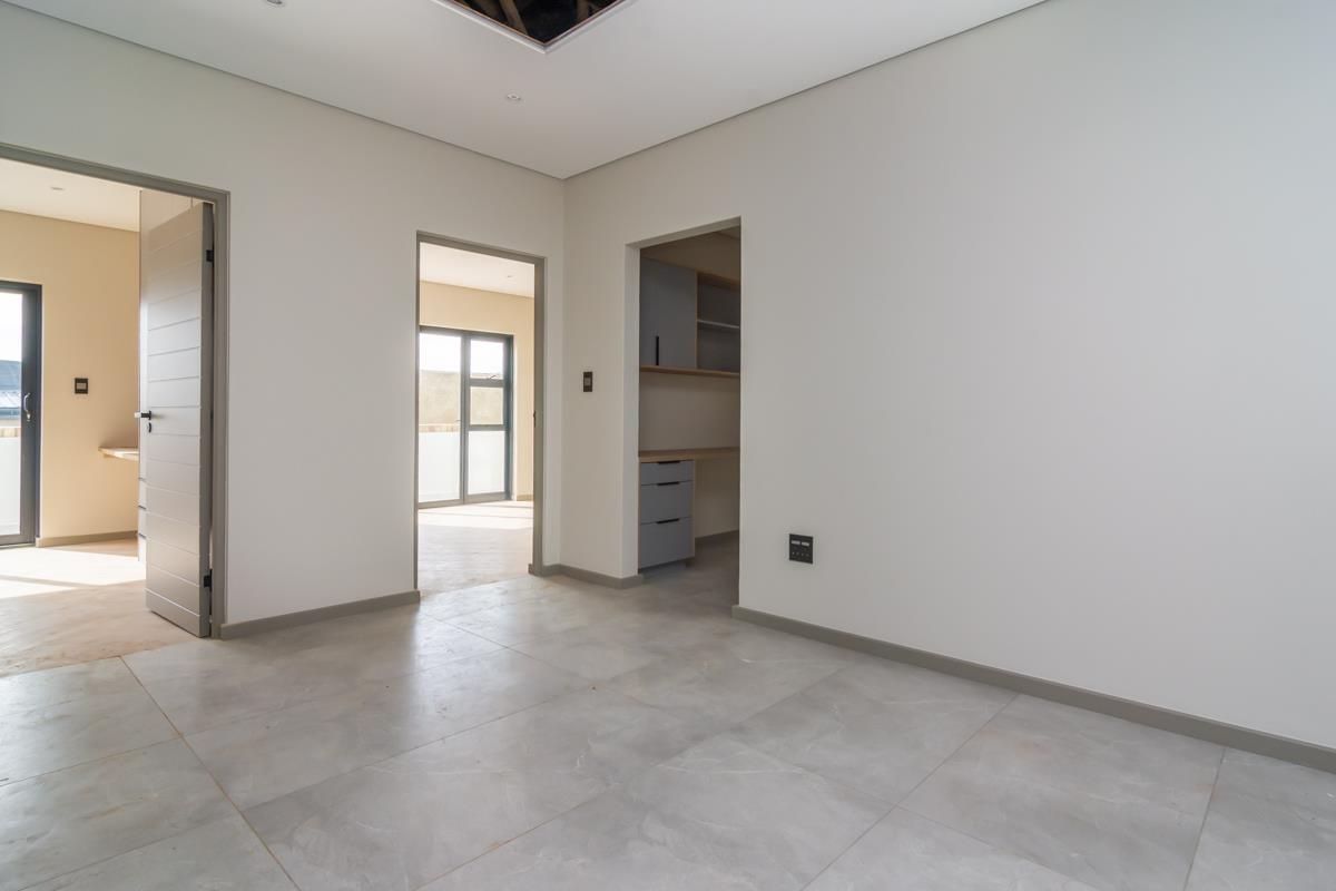 A bright, modern interior space featuring large format floor tiles, neutral walls, and a built-in study or utility nook.