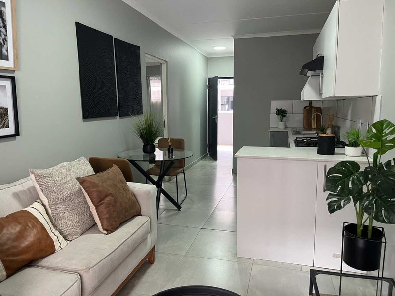Modern open-plan living area featuring a compact kitchen with built-in cabinetry, gas hob, extractor fan, and neutral tiled flooring throughout.