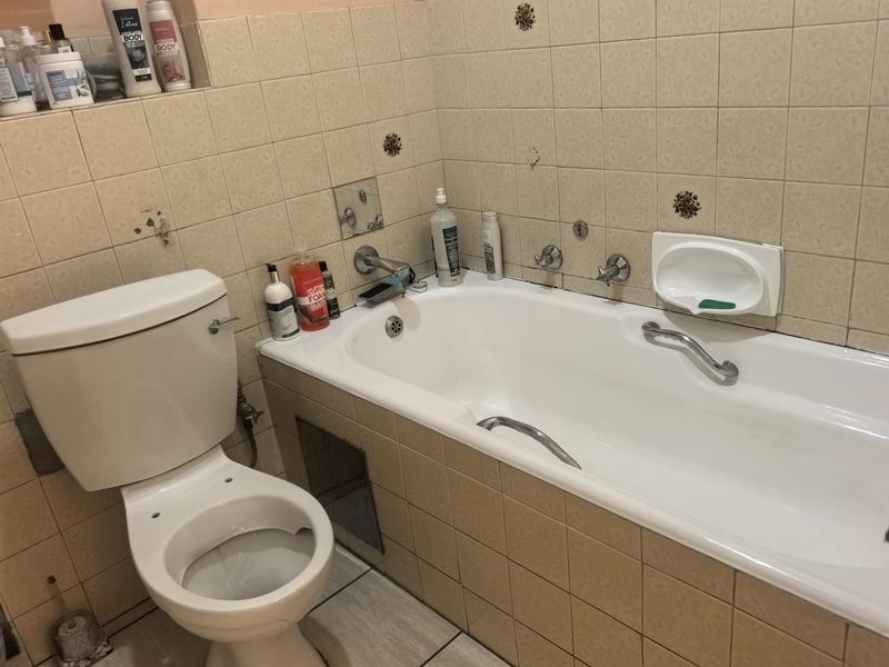 A dated bathroom featuring a standard bathtub, toilet, and tiled finishes. The space requires cosmetic updates and repairs to the wall tiling.