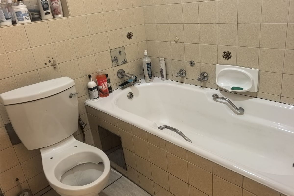 A dated bathroom featuring a standard bathtub, toilet, and tiled finishes. The space requires cosmetic updates and repairs to the wall tiling.
