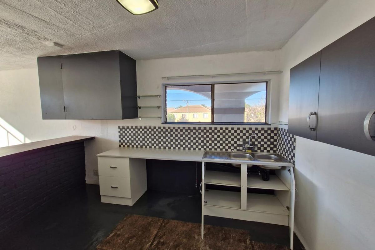 A dated kitchen area featuring dark cabinetry, a checkerboard backsplash, a double stainless steel sink, and a breakfast bar counter.