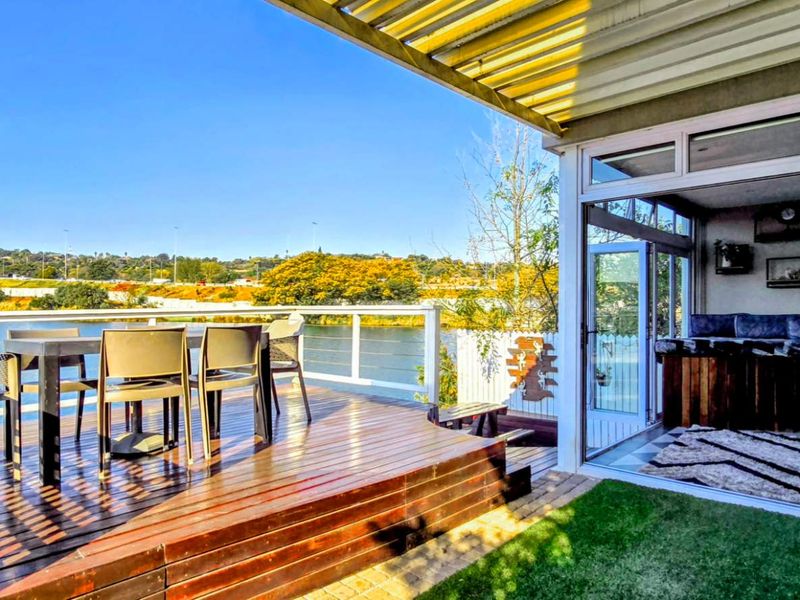 Spacious outdoor patio featuring timber decking, a pergola, and bi-fold doors connecting to an indoor living area, overlooking a scenic waterfront.