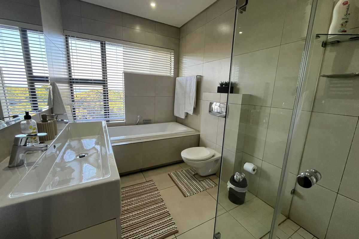 Modern bathroom featuring a built-in bathtub, wall-mounted toilet, glass-enclosed shower, and a sleek vanity basin with large format wall and floor tiling.