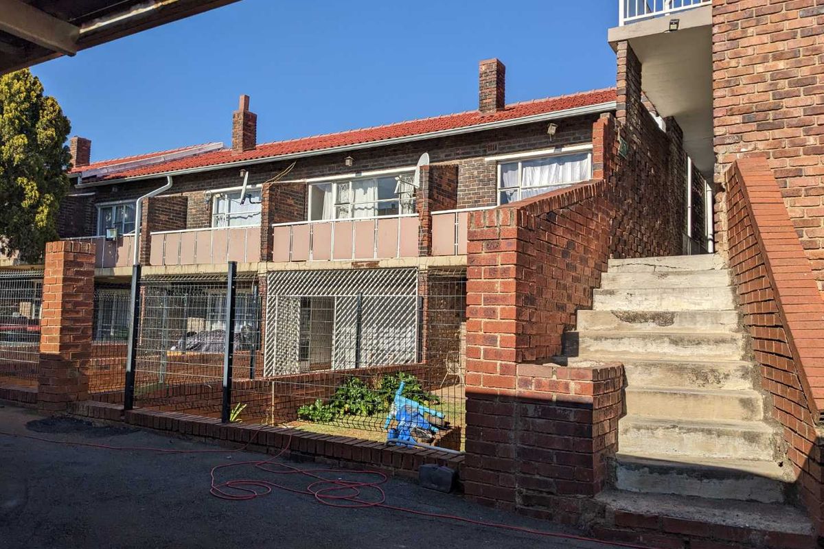 Rear view of a multi-level townhouse complex featuring exposed brick facade, tiled roofing, and an external concrete staircase leading to upper units.