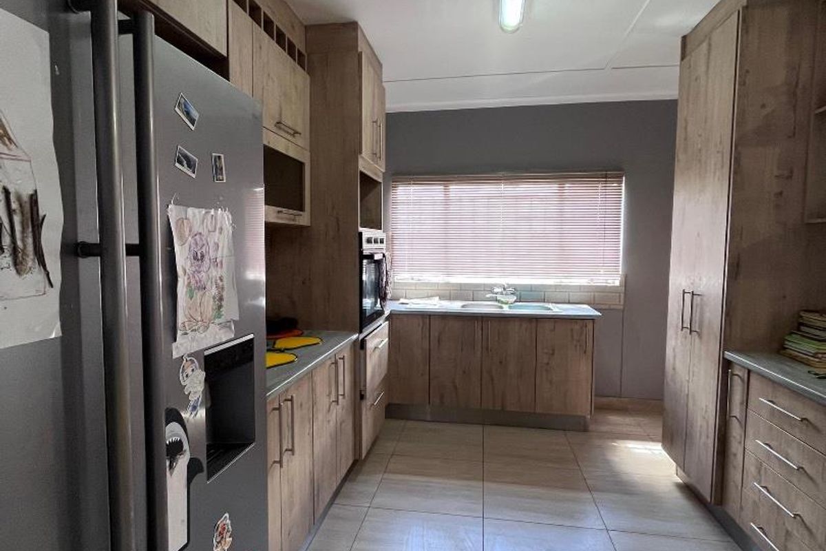 A functional galley-style kitchen featuring wood-look cabinetry, tiled flooring, built-in oven, and a window with blinds providing natural light.