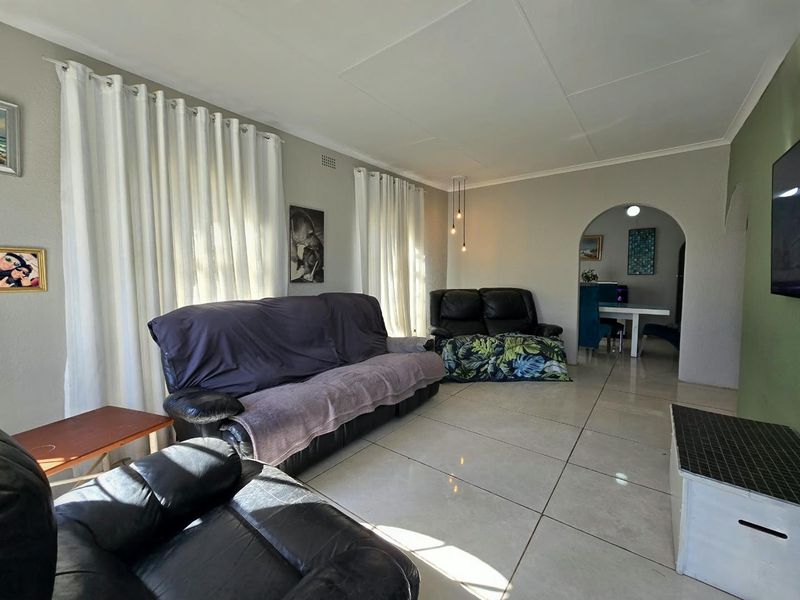 A spacious living room featuring large format floor tiles, a coved ceiling, and an arched entryway leading to the adjacent dining area.