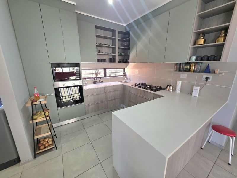 Modern kitchen featuring sage green and wood-grain cabinetry, stone countertops, built-in oven, gas hob, and tiled flooring with a functional breakfast bar layout.
