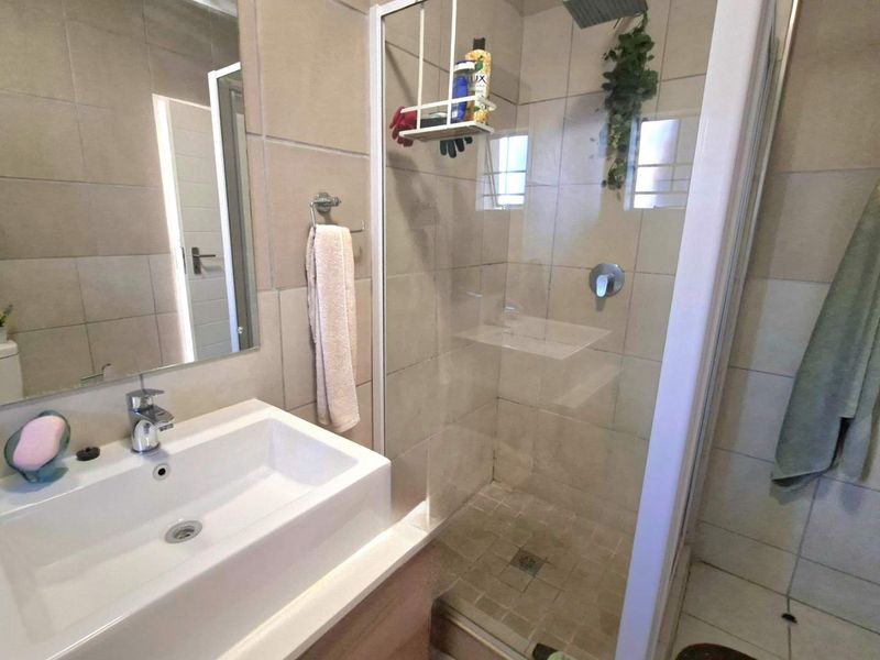 A functional bathroom featuring a modern vanity basin, wall-mounted mirror, and a tiled shower enclosure with a glass door.
