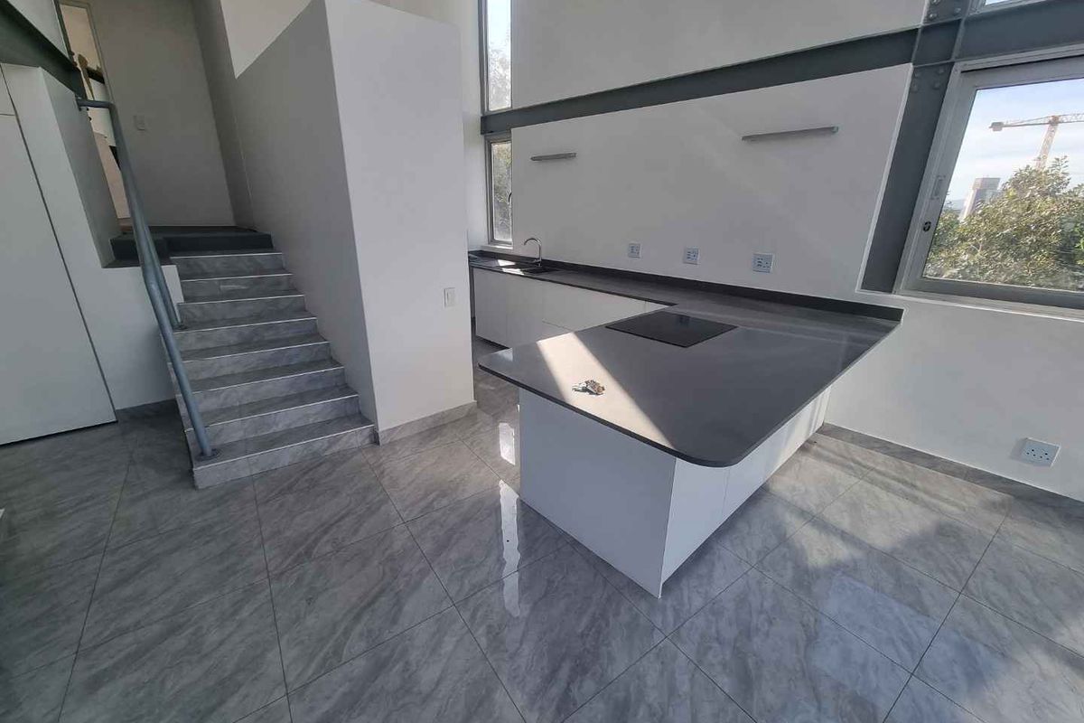 Modern penthouse kitchen featuring sleek cabinetry, stone countertops, integrated hob, and large windows, adjacent to a tiled staircase in an open-plan layout.