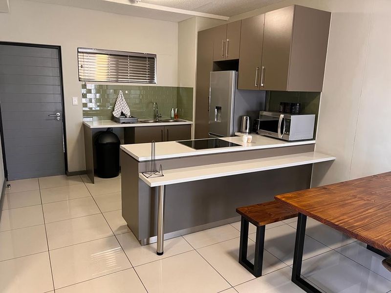 Modern kitchen featuring sleek cabinetry, stone countertops, a subway tile backsplash, and integrated hob, set against polished ceramic tile flooring.