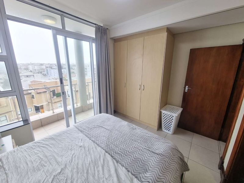 A bright bedroom featuring built-in cupboards, tiled flooring, and a sliding glass door providing direct access to a private balcony with city views.