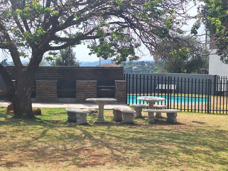 Communal outdoor area featuring a swimming pool, brick built-in braai, and paved surrounds, set within a landscaped garden space.