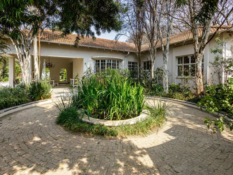 A charming front entrance featuring a circular cobblestone driveway, a central garden bed, and a covered patio area with a tiled roof.