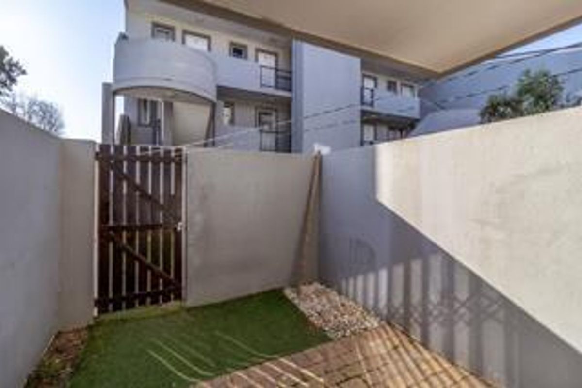 A private courtyard area featuring a timber gate, paved section, and artificial turf, providing a secure outdoor space for the apartment.