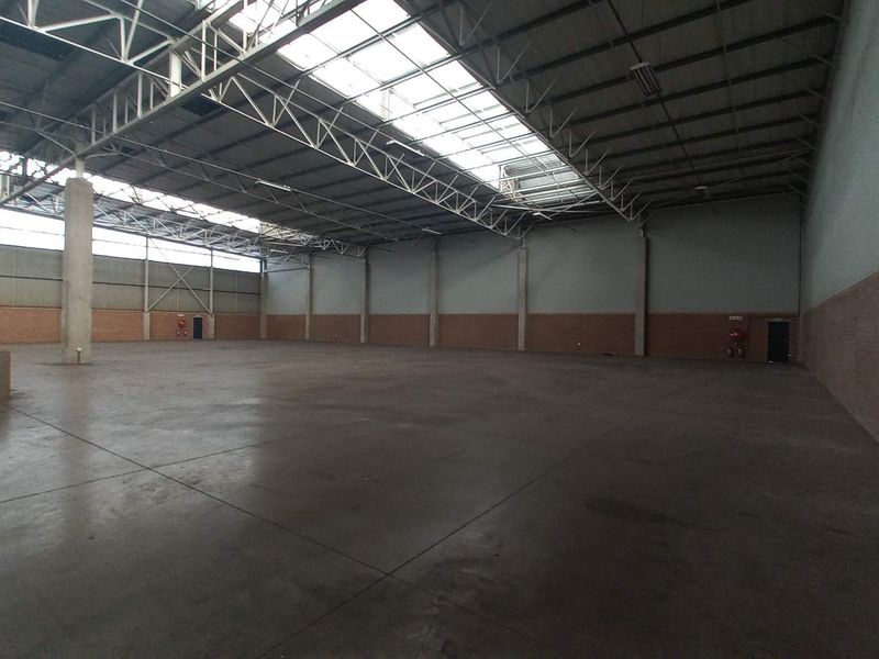 Spacious industrial warehouse unit featuring high ceilings with skylights, concrete flooring, and exposed steel truss roofing, suitable for storage or manufacturing operations.