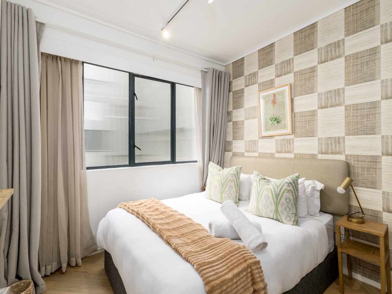 A well-maintained bedroom featuring textured wallpaper, timber flooring, and a window with fluted glass for privacy.