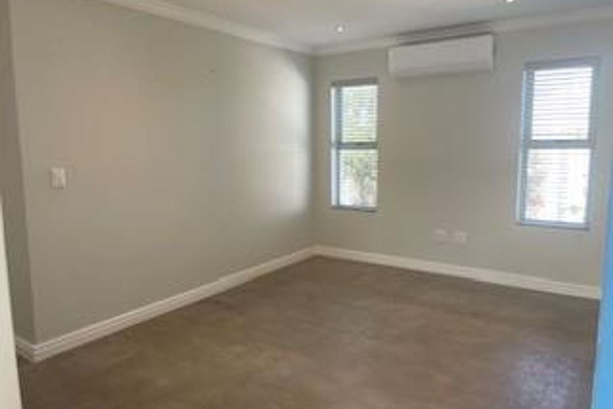 A clean, empty bedroom featuring neutral walls, tiled flooring, recessed lighting, and a wall-mounted air conditioning unit.