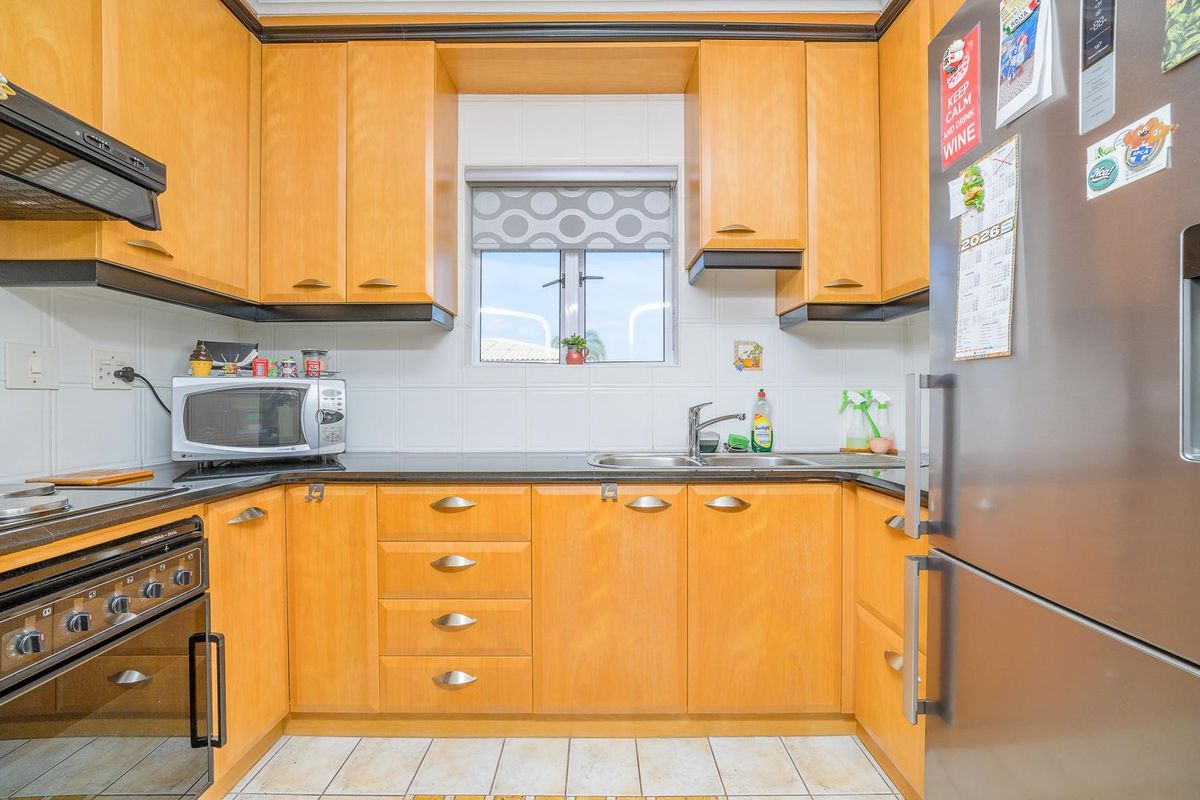 Compact kitchen featuring light wood-toned cabinetry, dark countertops, tiled backsplash, and integrated stainless steel oven and extractor fan.