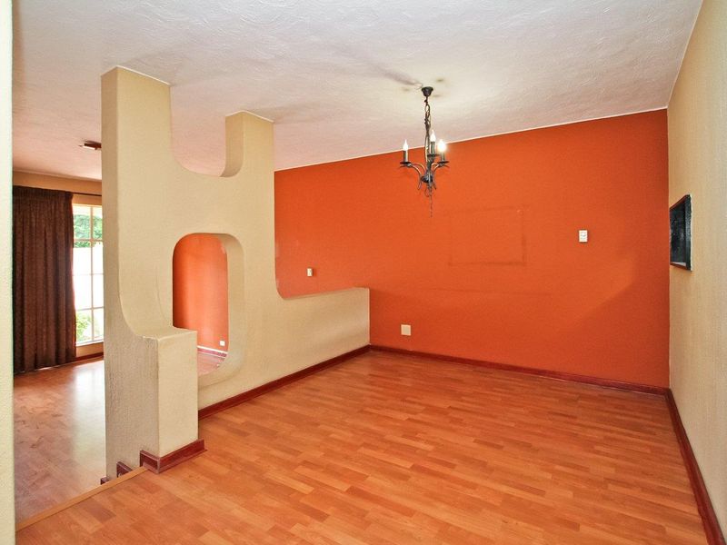 An empty living area featuring laminate flooring, a unique decorative partition wall, and a wrought iron chandelier, ready for a modern update.