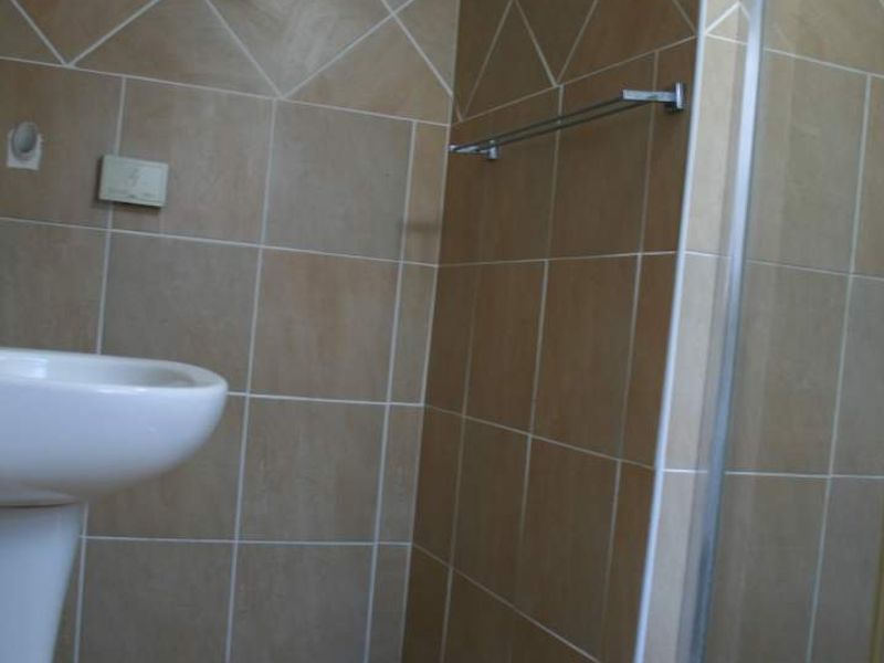 A functional bathroom featuring a pedestal basin, tiled walls and flooring, and a glass-enclosed shower unit.